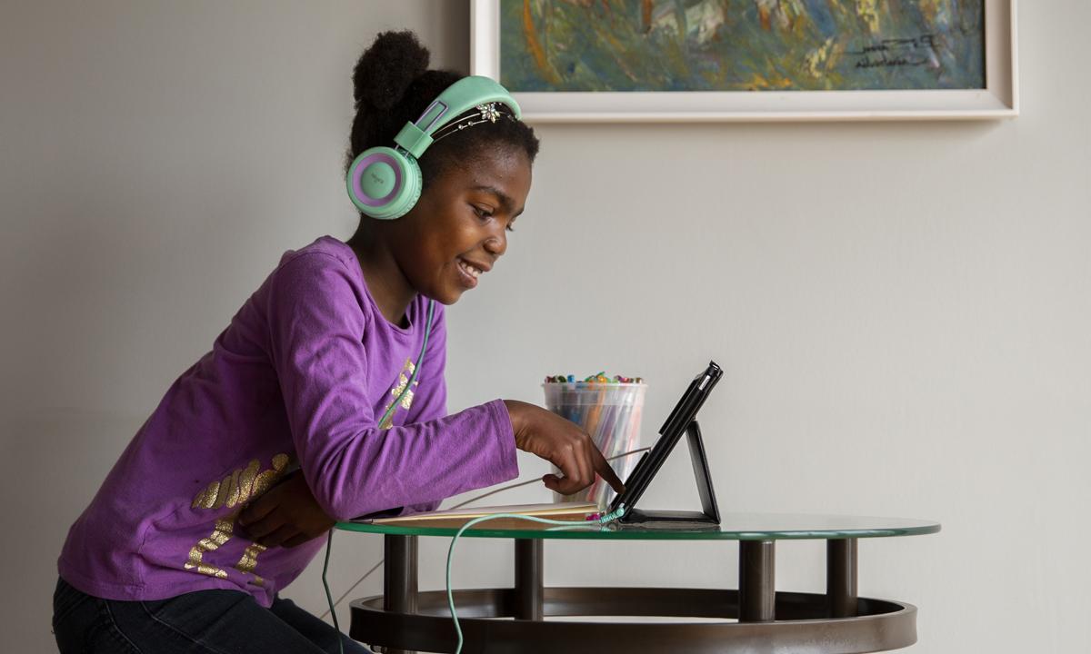 Image of a young child sitting in front of a computer with headphones on and smiling