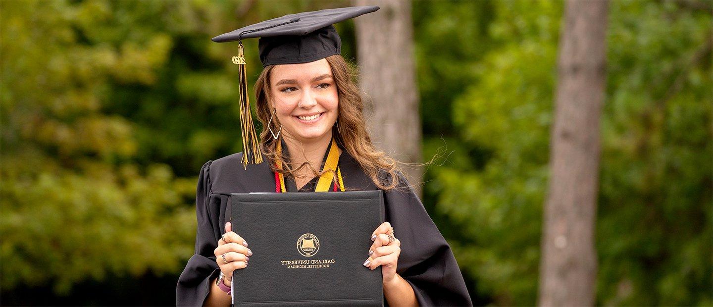 一位365英国上市官网的女毕业生，戴着帽子，穿着长袍，手里拿着一张文凭.