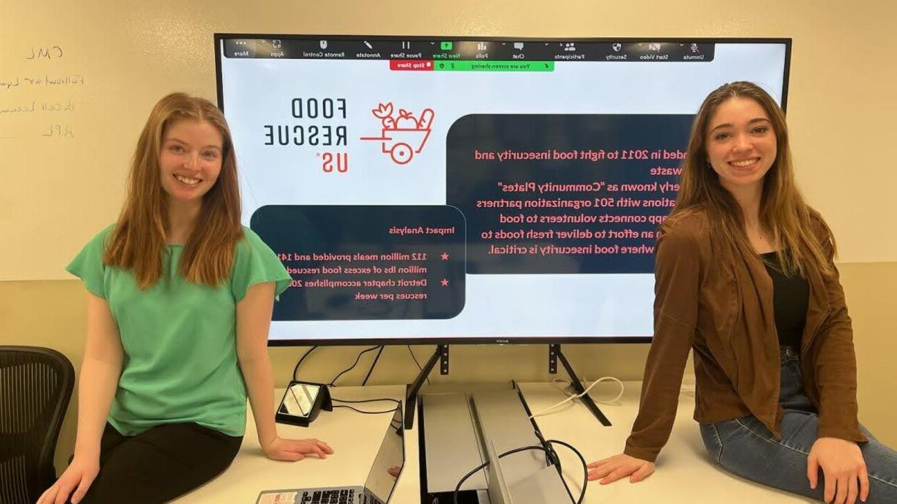 365英国上市官网学生, 莎拉·奈奎斯特和瑞秋·惠伦, 坐在一个大显示器前，上面显示着美国食品救援组织的信息.